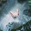 high-angle photography of woman bathing below waterfalls during daytime