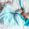 baby in teal onesie lying on bed